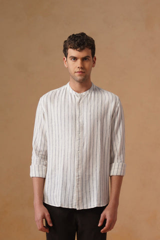 Man wearing a light-colored shirt and dark pants against a beige wall.