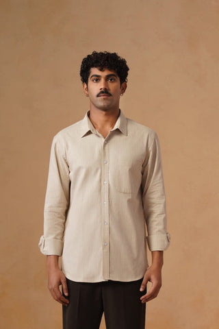 Man wearing a beige shirt and dark pants standing against a beige wall.