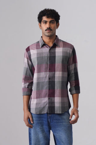 Man wearing a plaid shirt and jeans standing against a plain background