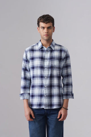 Man wearing a blue and white plaid shirt and jeans standing against a plain background